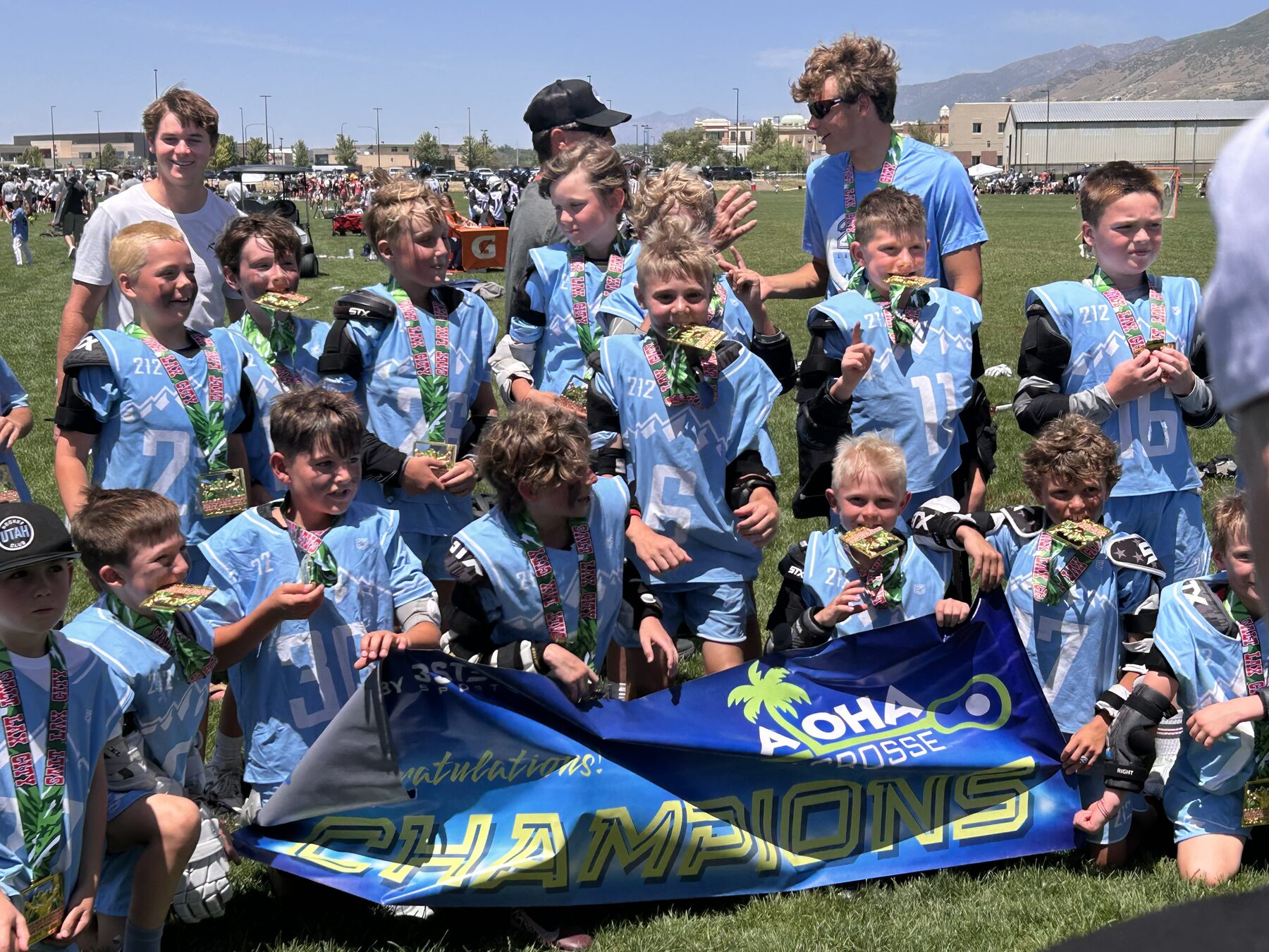 212 Lacrosse team celebrating behind an Aloha Lacrosse CHAMPIONS banner with medals